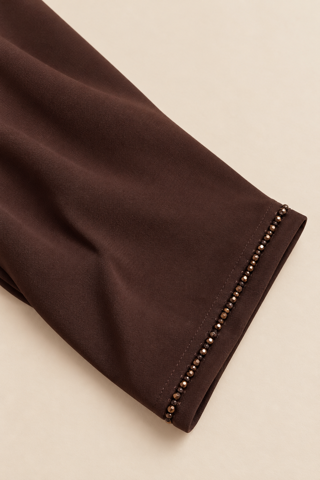 Gros plan sur la bordure perlée et la couture du poignet de l’abaya chocolat
