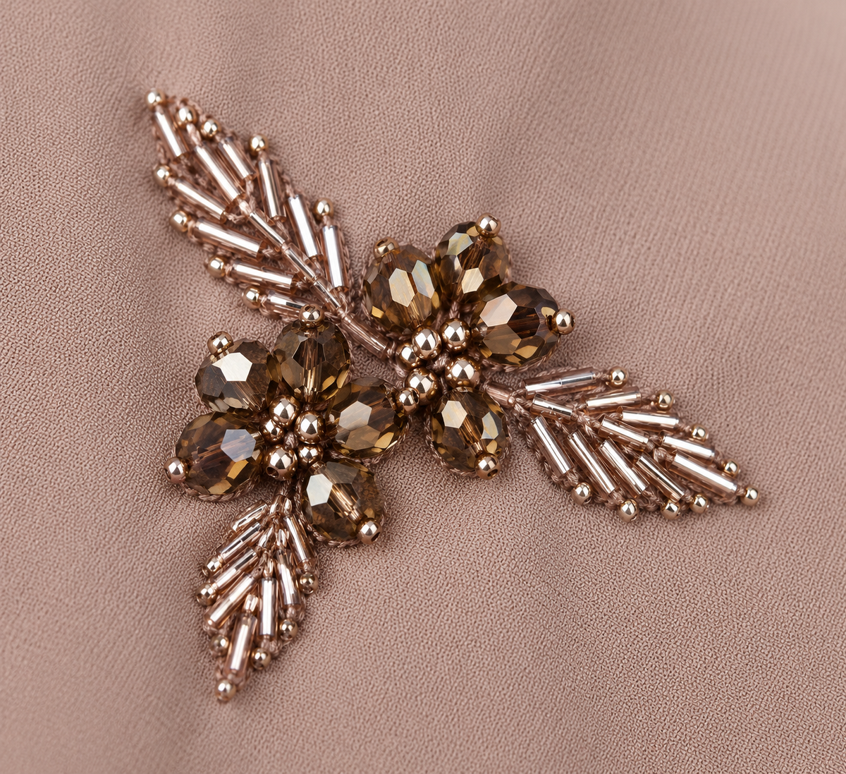 Détail du motif floral perlé bronze sur l’abaya taupe rosé
