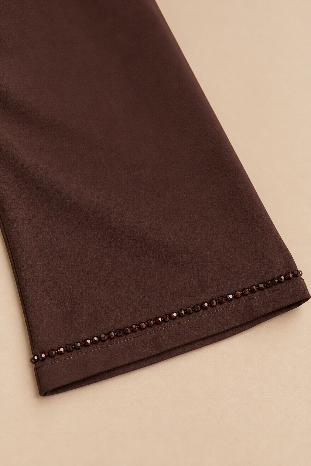 Détail de la manche chocolat : bordure de perles facettées et finition cousue.
