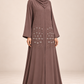Abaya Bourgeons taupe portée de trois quarts, coupe longue et manches à bordure perlée.