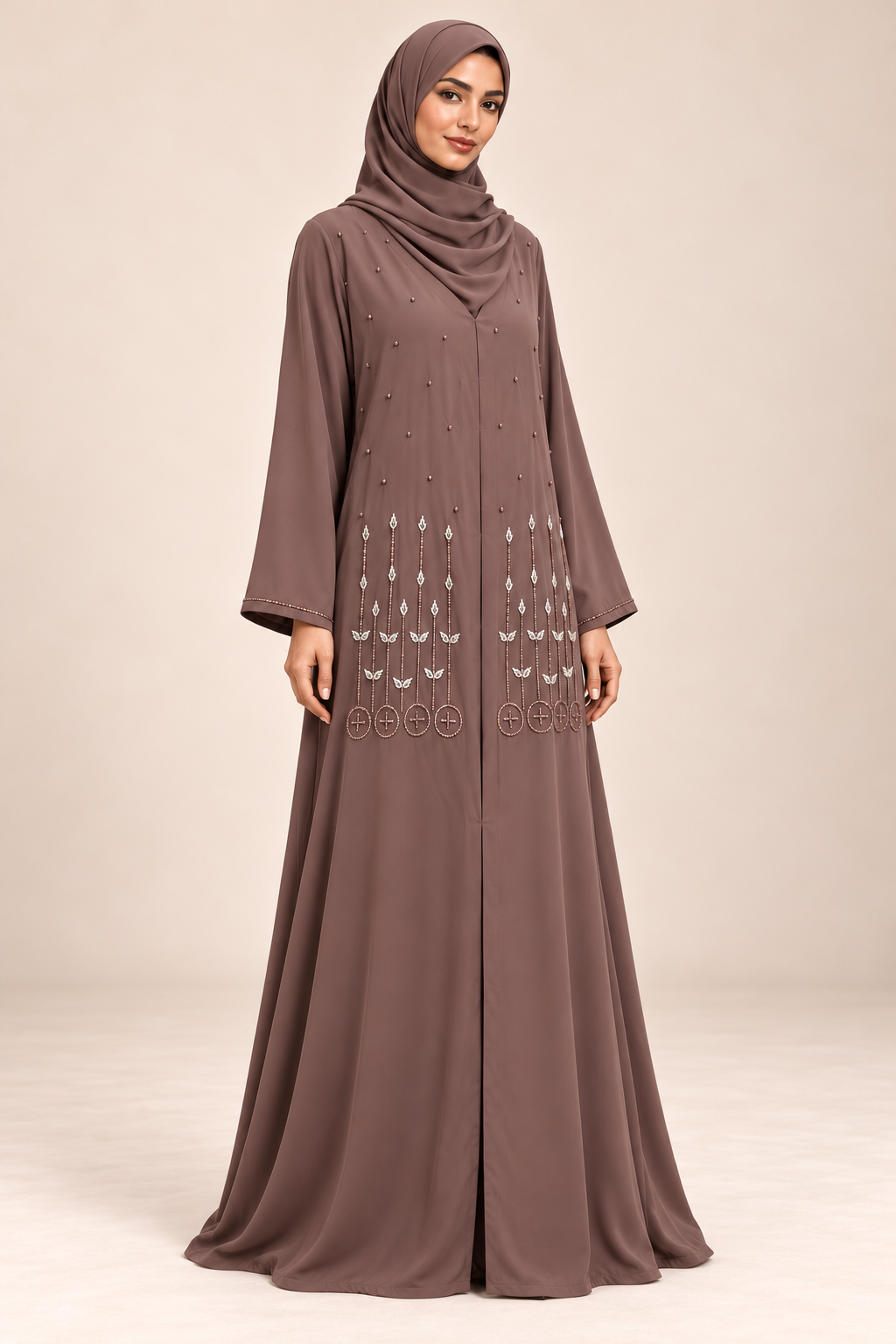 Abaya Bourgeons taupe portée de trois quarts, coupe longue et manches à bordure perlée.