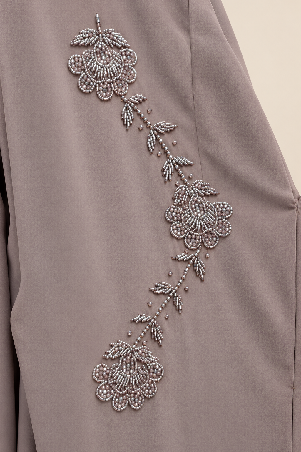 Gros plan des fleurs et feuilles perlées aux reflets argentés de l’abaya Roseraie taupe